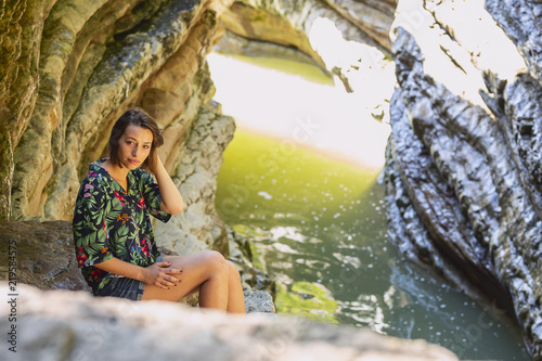 A girl sitting on the big gray Rock in the mountains near the river.