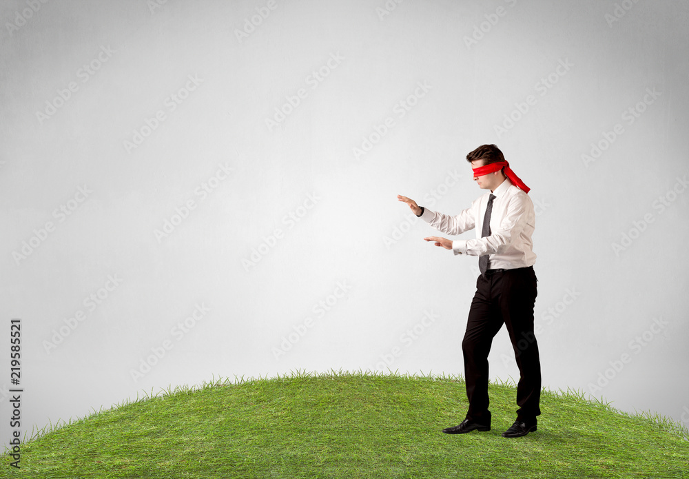Young blindfolded businessman steps on a patch of grass Young blindfolded businessman steps on a patch of grass