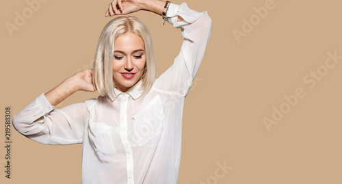 Attractive girl in white shirt dancing. Young woman having fun, beige wall on background. Studio portrait of beautiful blonde hair model. Concept of party and fun.