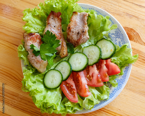 A plate of vegetables and meat. Cucumber, tomato, lettuce.