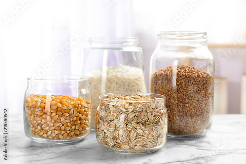 Jars with different types of grains and cereals on table
