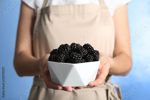 Woman holding bowl of fresh blackberry against color background, closeup
