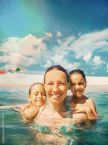 Mother and daughter swim in the shallow sea. They laugh and enjoy on a beautiful beach.