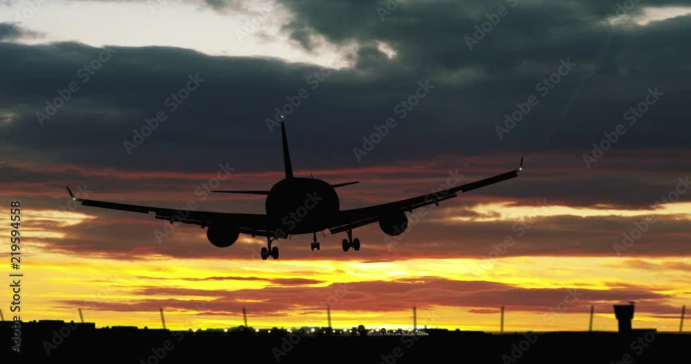 Jet airplane silhouette landing at the airport during sunset. Clouds, shape of plane, fence and flashing runway lights.