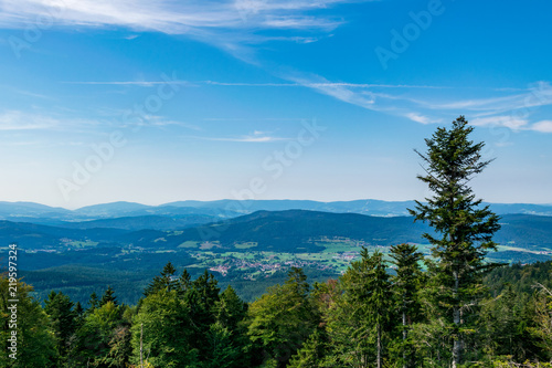 View from top of a mountain in the valley with clouds on the sky and mountains on the background and stones and trees in front of in the bavarian forest