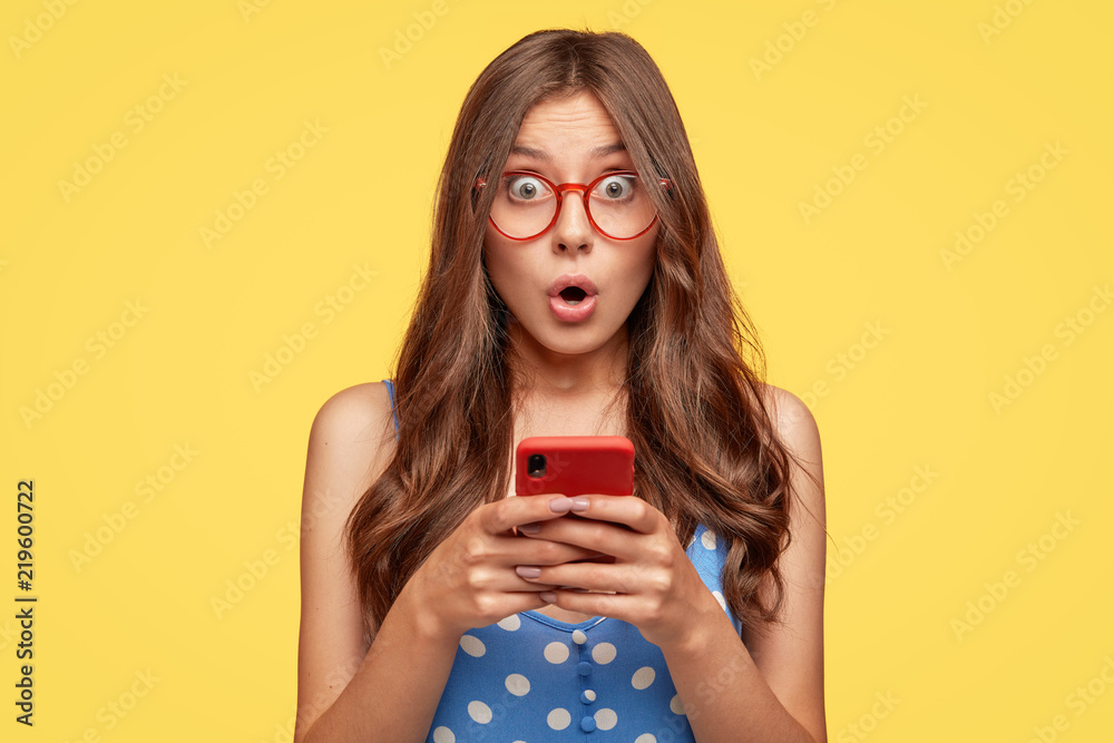 Surprised Young Female Model Holds Modern Cell Phone Reads Sudden News On Internet Web Page Surfes In Social Networks Poses Against Yellow Background People Emotions Technology Lifestyle Stock Photo Adobe Stock