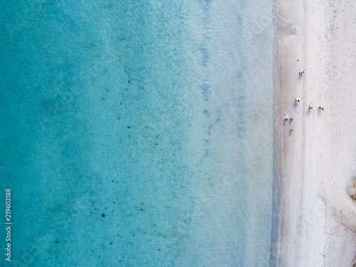 Aerial view of some people walking on a white beach bathed by a beautiful turquoise sea. Cala Brandinchi, Sardinia, Italy.