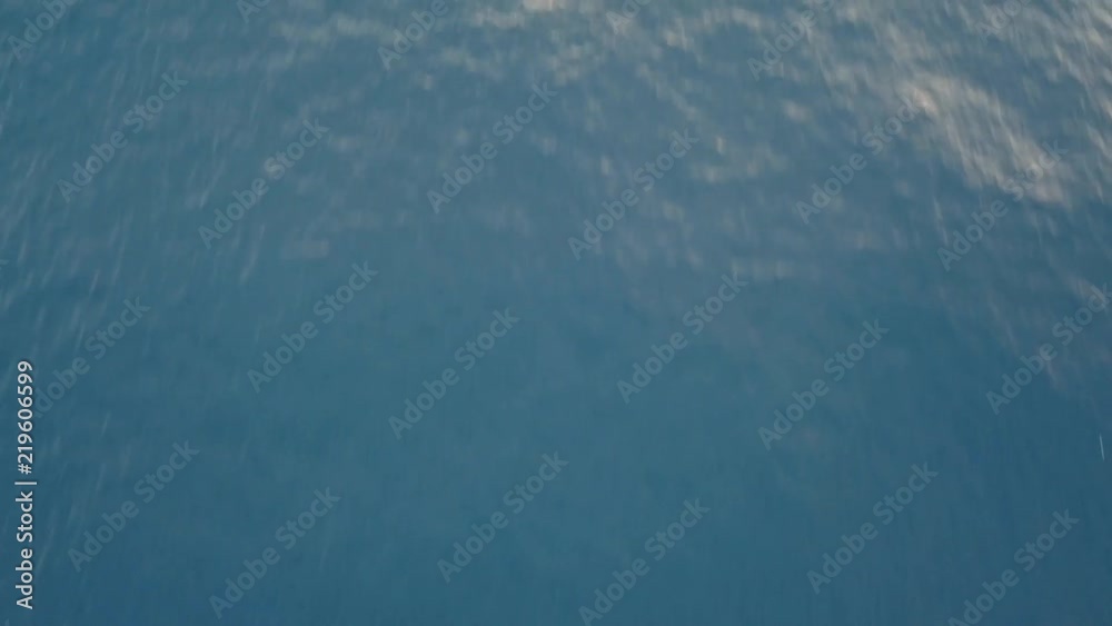 Moving forward over blue ocean water, camera tilting up discovering beautiful landscape with volcano on sunset mountain background