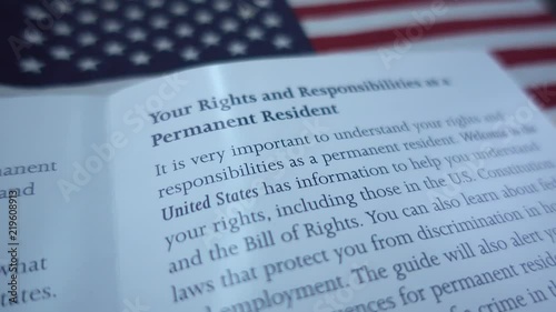Fragment of Public Guide of Right and Responsibilities as Permanent Resident of USA on blurred American flag background. 