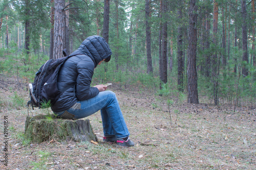 A woman sits on a stump in the woods early in the morning and checks her cellphone. A female hiker, backpacker trekking in the woods and mountains. Healthy lifestyle adventure, camping on hiking trip