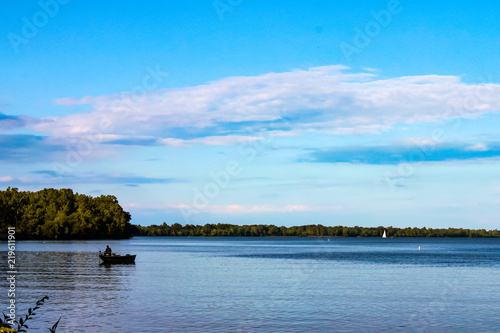 Fisherman in boat on lake with sailboat in the distance  - Lake Erie photo