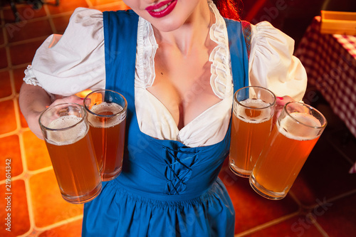 Young beautiful girl holds four glasses of beer in hands at celebration of oktoberfest. Beer glasses on the background of the female breast.
