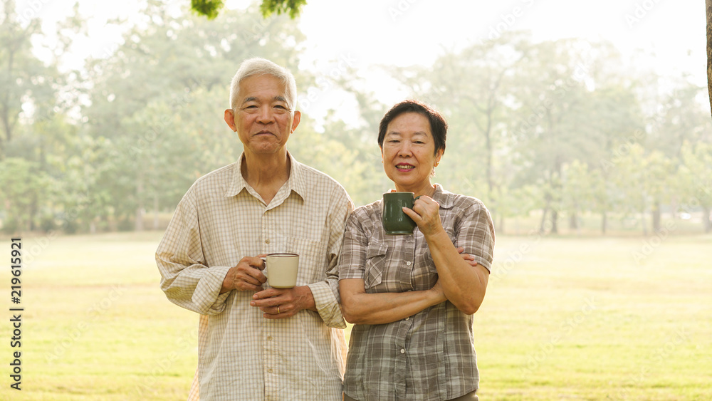Asian elderly couple drink tea coffee in moring park sun light