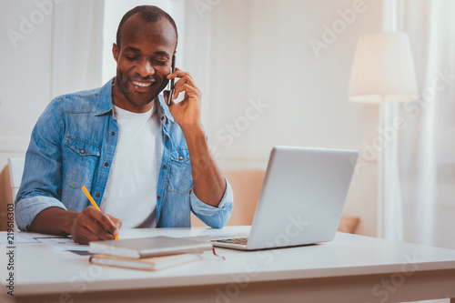 Taking notes. Content afro-american man talking on the phone and taking some notes