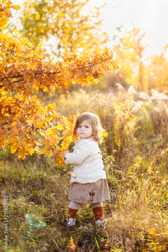 Adorable little girl wearing beige coat among autumn trees. Autumn forrest walk. Golden autumn time
