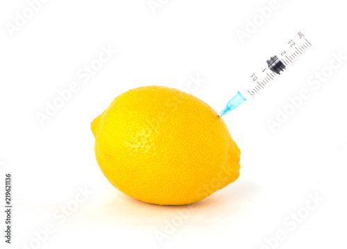 Lemon on a white background in which syringe is injected with gmo and nitrates, close-up, genetically modified organism photo