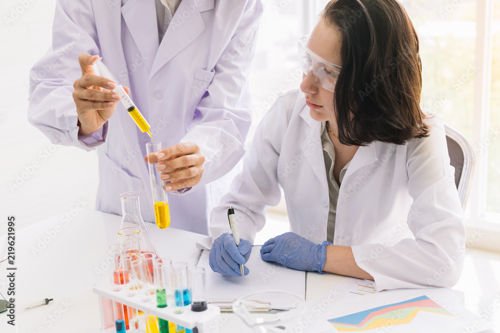 Young woman scientist in the lab was taking notes of test results showing a yellow fluorescent test tube with colleagues who were dripping liquid. Young woman scientist in the lab was taking notes of test results showing a yellow fluorescent test tube with colleagues who were dripping liquid.