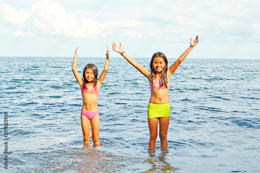 Two happy young girls playing with the water in the sea