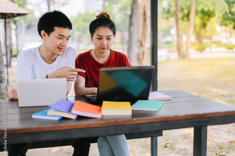 Group of asian university students reading a book the final exam by a tablet and a laptop on a wooden table.Technology and Education Concepts. Group of asian university students reading a book the final exam by a tablet and a laptop on a wooden table.Technology and Education Concepts.