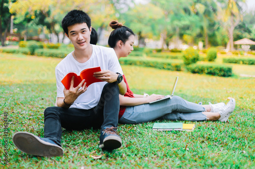 Group of asian university students reading a book the final exam together on grass field at outdoors.Educational Learning Concepts. photo