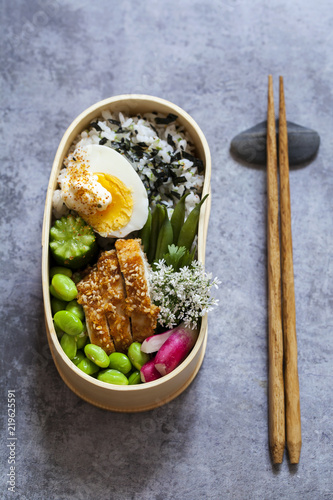 Japanese bento lunch box with sesame crusted chicken, edamame beans, egg and spicy rice