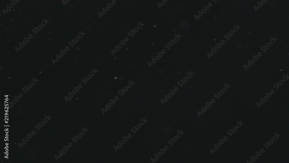 Slow motion backlit dust particles floating in the air on a black background under flickering light