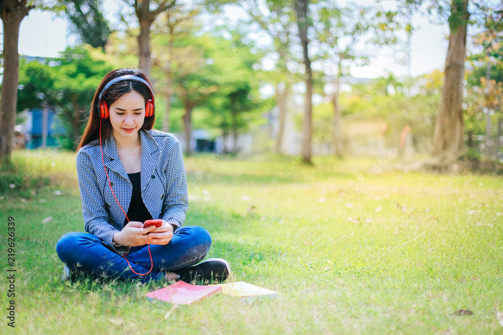 Asian student with headphones relaxing on the green grass.She is listening to music using a smertphone,chill out and leisure. Asian student with headphones relaxing on the green grass.She is listening to music using a smertphone,chill out and leisure.