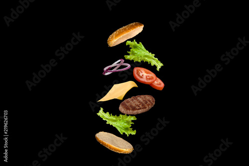 Delicious burger with flying ingredients isolated on black background.