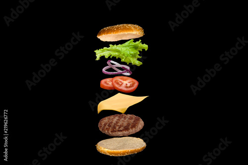 Fotografia Delicious burger with flying ingredients isolated on black background