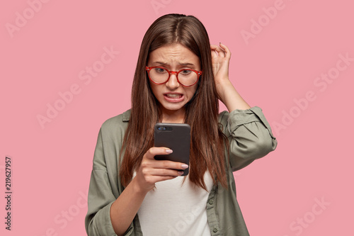 Quadro su tela Nervous puzzled woman scratches head in bewilderment, reads bad news at internet