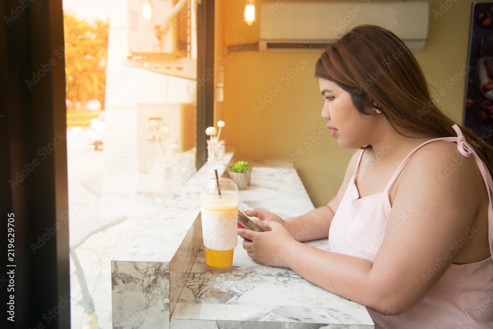 Portrait of Pretty Asian fat woman drinking orange juice and used mobile in a coffee shop. Portrait of Pretty Asian fat woman drinking orange juice and used mobile in a coffee shop.