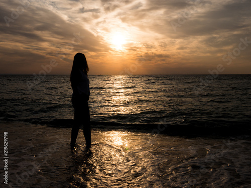 Silhouette of a young girl on the beach. young girl is walking at sunset by the sea. Tourist girl on beach during vacation © DC Studio