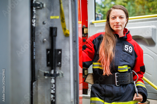 Photo of fire woman with long hair in overalls stands in fire engine