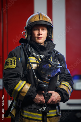 Photo of young fireman wearing helmet with gas mask on background of fire engine © Sergey