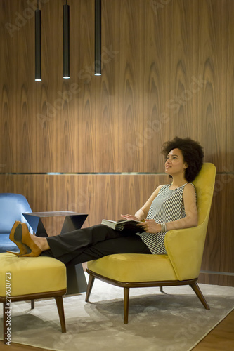 Young woman sittinh on a yellow chair and reading a book photo