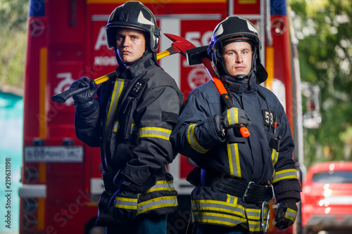 Photo of two firemen with axes in hands near fire engine © Sergey
