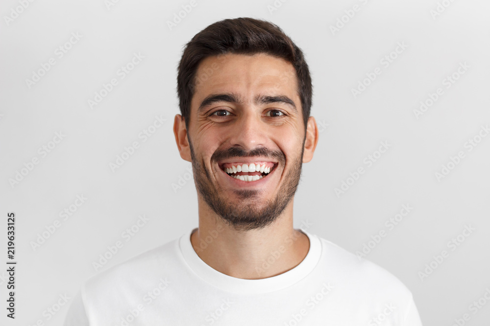 Close up shot of handsome smiling unshaven young man in white t-shirt laughing out loud Close up shot of handsome smiling unshaven young man in white t-shirt laughing out loud