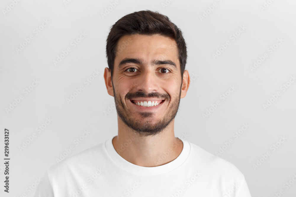 Close up portrait of smiling attractive man in white t-shirt isolated on gray background Close up portrait of smiling attractive man in white t-shirt isolated on gray background