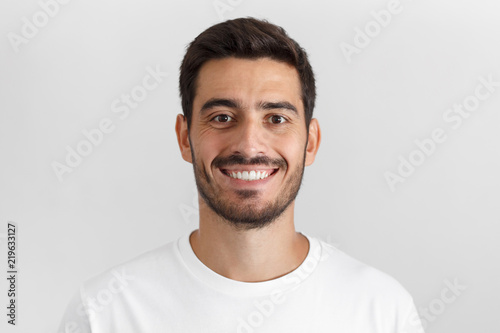 Close up portrait of smiling attractive man in white t-shirt isolated on gray background