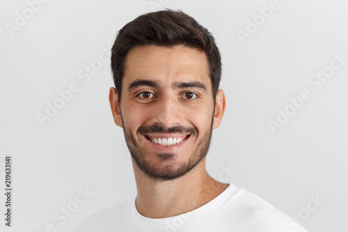 Closeup photo of young smiling handsome european man isolated on gray background, dressed in white casual t-shirt