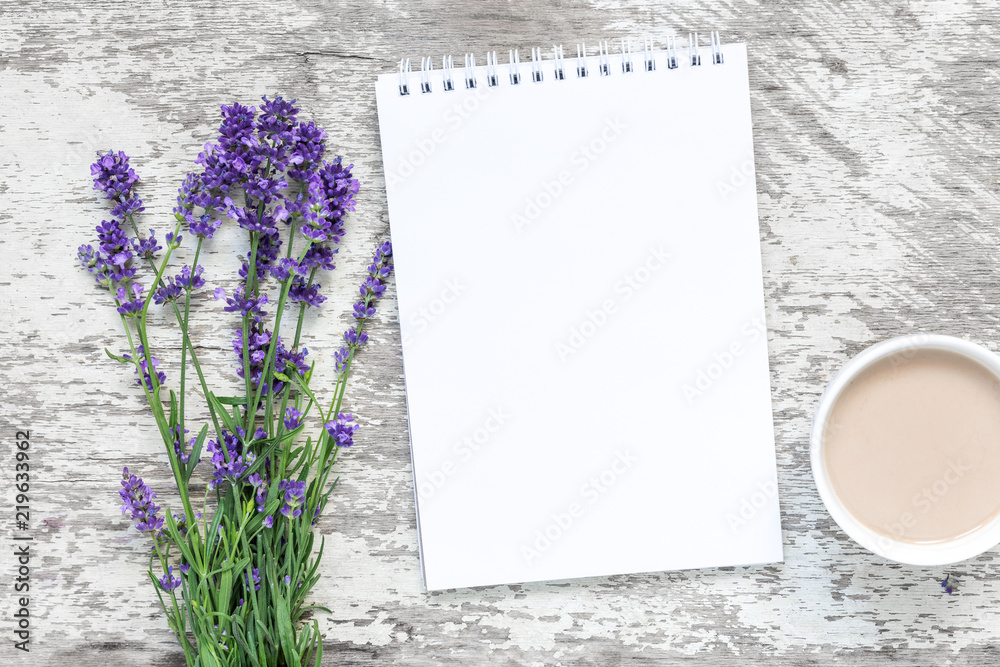 Obraz premium bukiet kwiatów lawendy z pustym białym notatnikiem i filiżanką cuppuccino na białym drewnianym stole. widok z góry. makieta