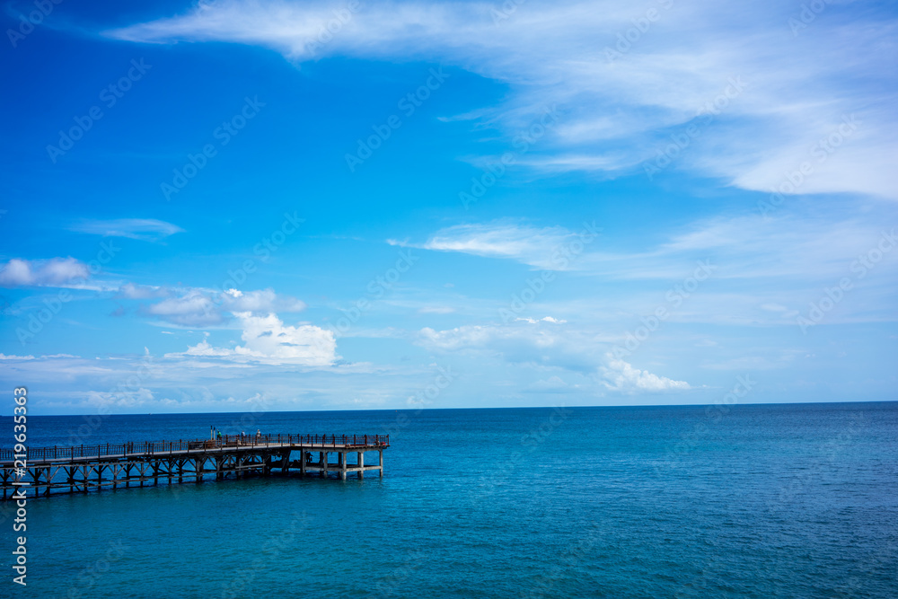 wood pier and calm ocean water with blue sky and clouds