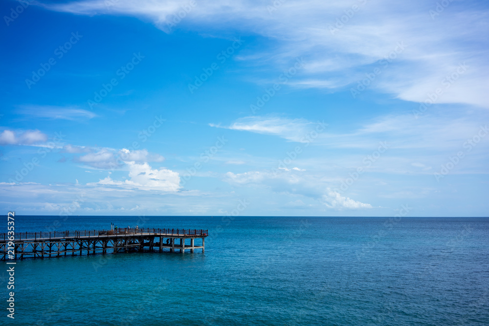 wood pier and calm ocean water with blue sky and clouds