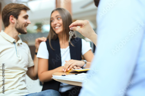 Close up of real estate agent giving keys to couple of customers.