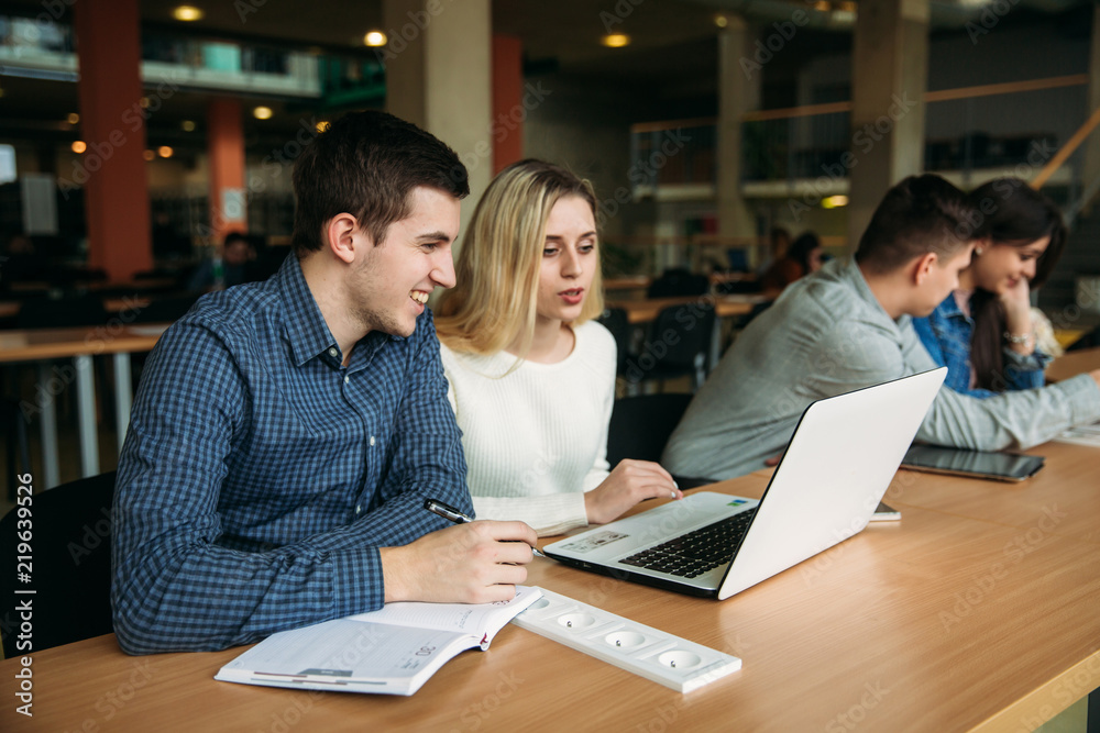Fototapeta premium Group of college students studying in the school library, a girl and a boy are using a laptop and connecting to internet