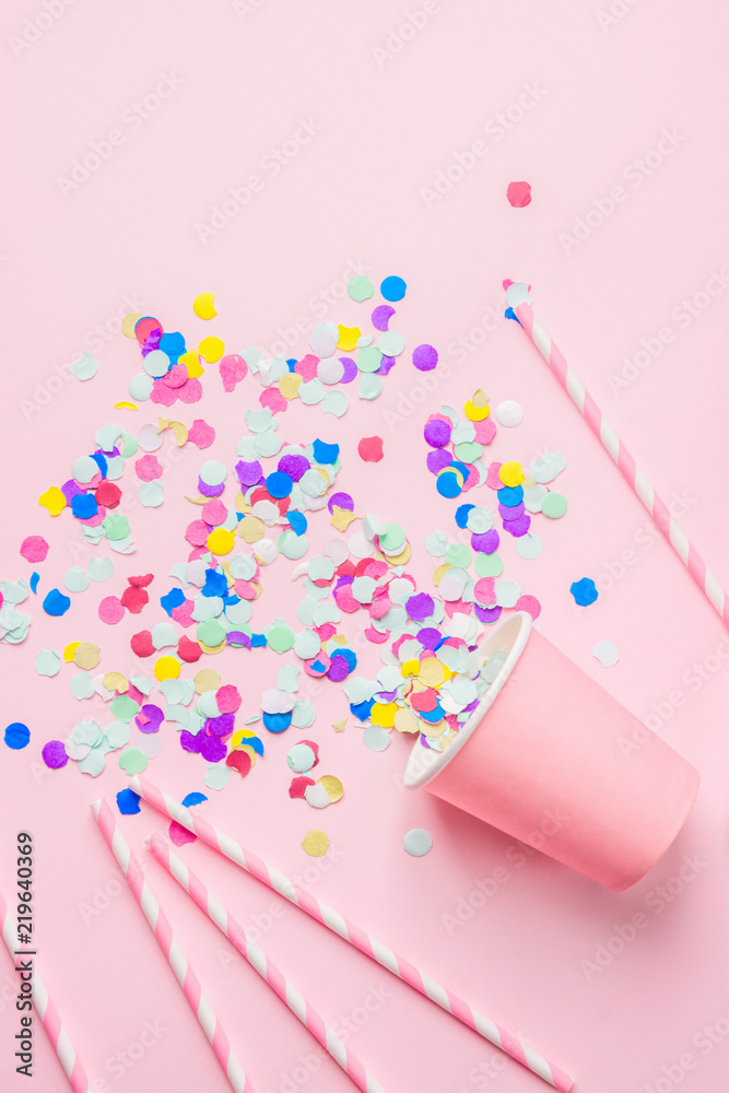 Drinking Paper Cup Striped Straws Colorful Confetti Scattered on Fuchsia Background. Flat Lay Composition. Birthday Party Celebration Kids Fun Cheerful Atmosphere. Greeting Card Poster Template