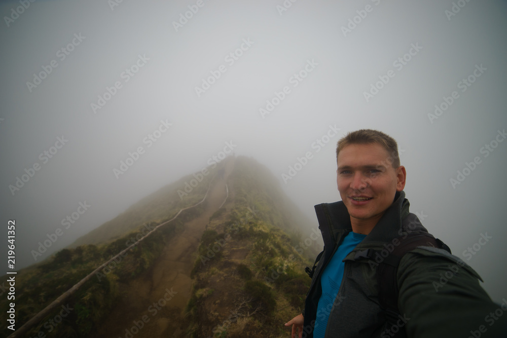 A person making selfie into the misty foggy road in forest road in a dramatic scene