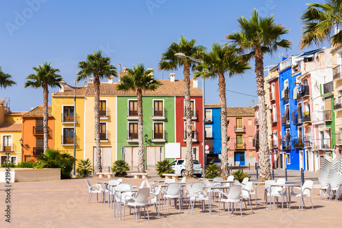 Old street with colorful houses, palm trees and outdoor cafe with white furniture.