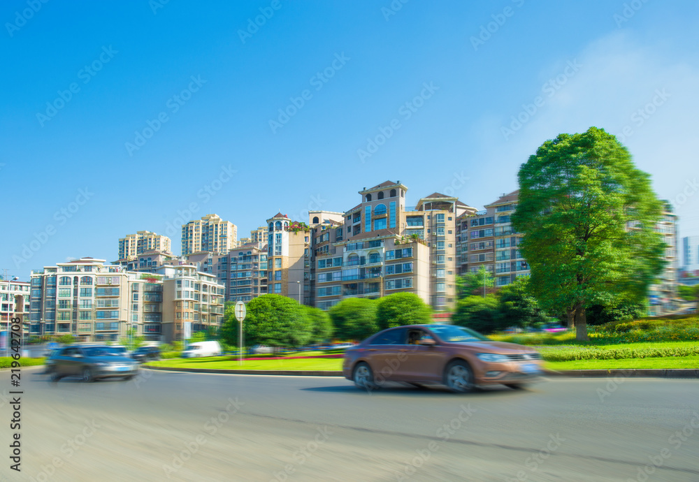 Modern urban landscape, high-rise buildings, lush parks, fast driving of various cars on asphalt roads, in sunny summer