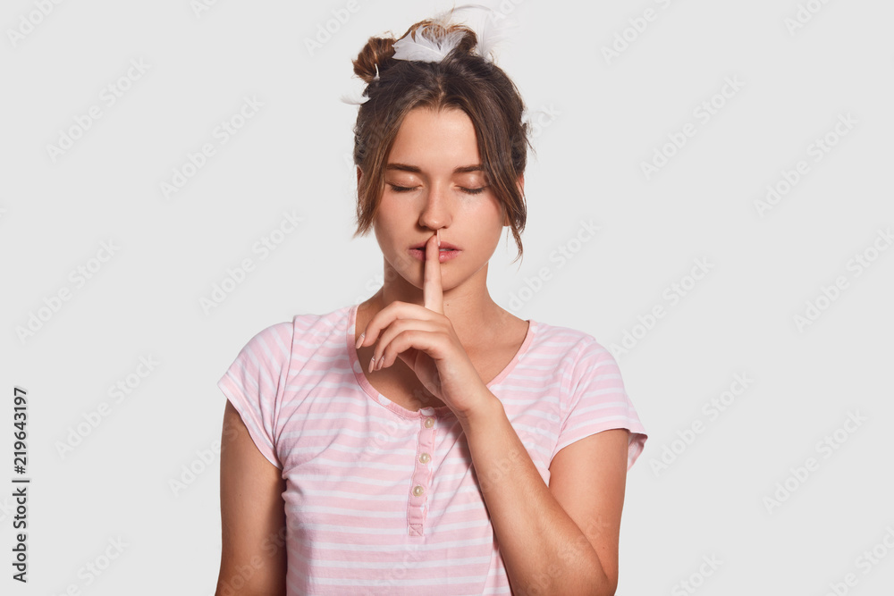 Be quiet, please! Serious attractive female asks not make noise and be speechless as someone is sleeping, makes hush gesture, has feathers on head, dark hair, dressed casually, keeps eyes shut Be quiet, please! Serious attractive female asks not make noise and be speechless as someone is sleeping, makes hush gesture, has feathers on head, dark hair, dressed casually, keeps eyes shut